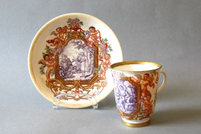 A Du Paquier cup with a saucer, painted with biblical scenes in rich, colourful cartouche frames with putti